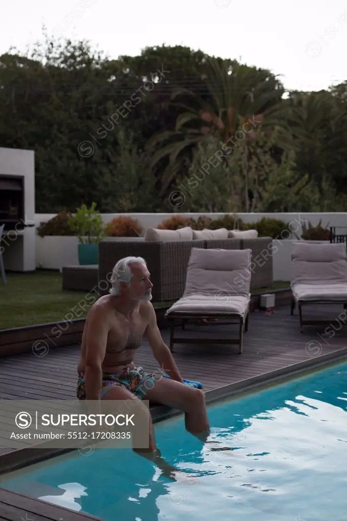 Active senior man sitting at the edge of swimming pool