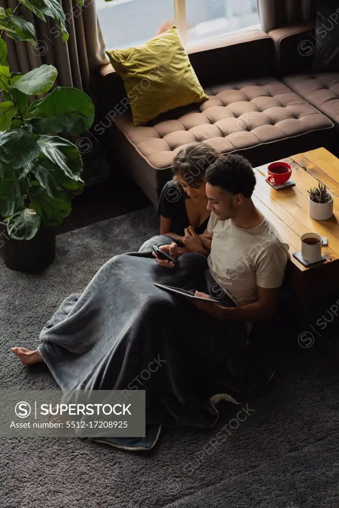 Couple using mobile phone and digital tablet in living room at home