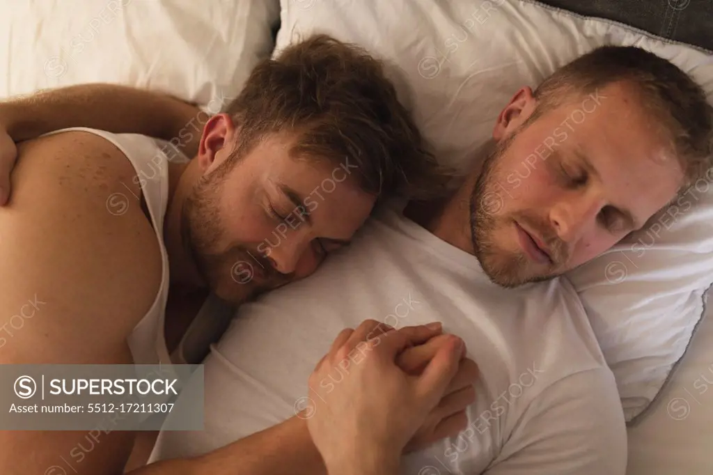 High angle view close up of Caucasian male couple relaxing at home, lying in a bed, embracing and sleeping together.