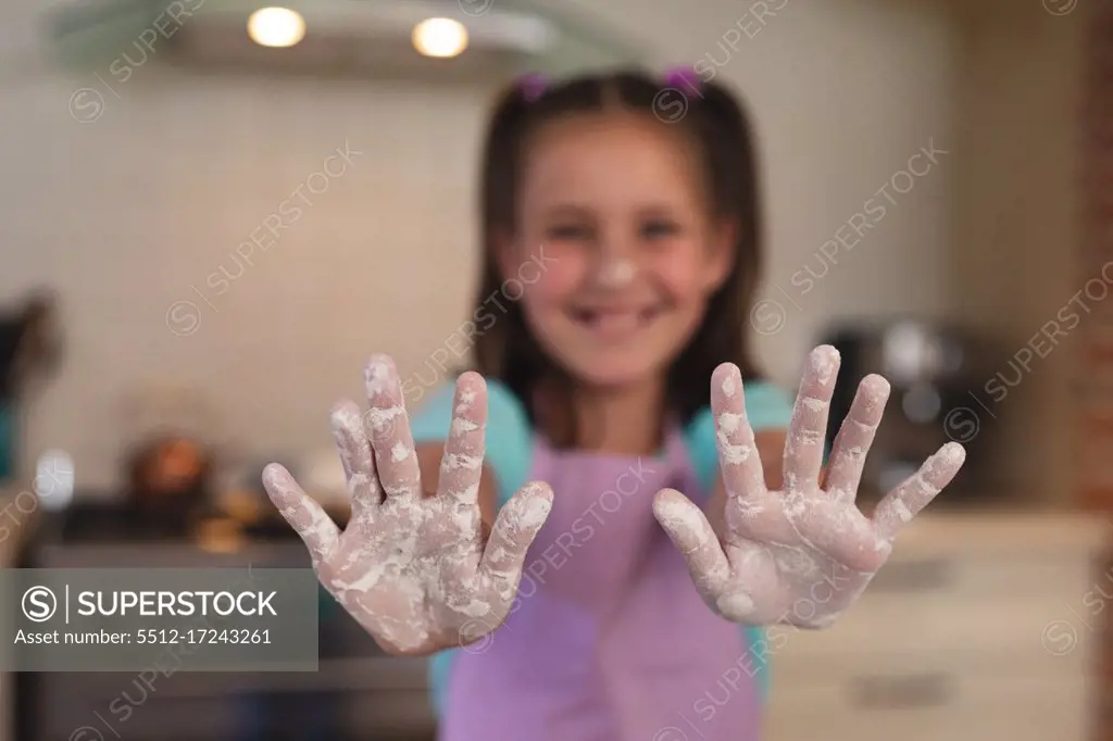 Portrait of caucasian girl in a kitchen, looking at camera and showing her hands with flour. self isolation at home during coronavirus covid 19 quarantine lockdown.
