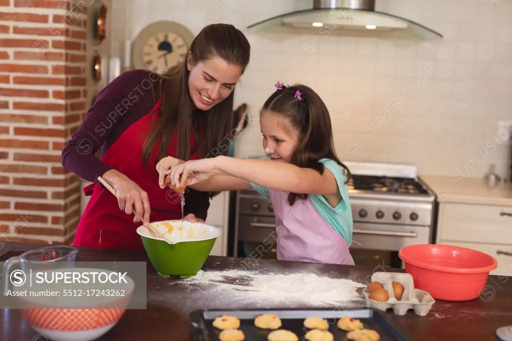 Caucasian woman with her daughter baking in a kitchen and wearing apron. self isolation at home during coronavirus covid 19 quarantine lockdown.