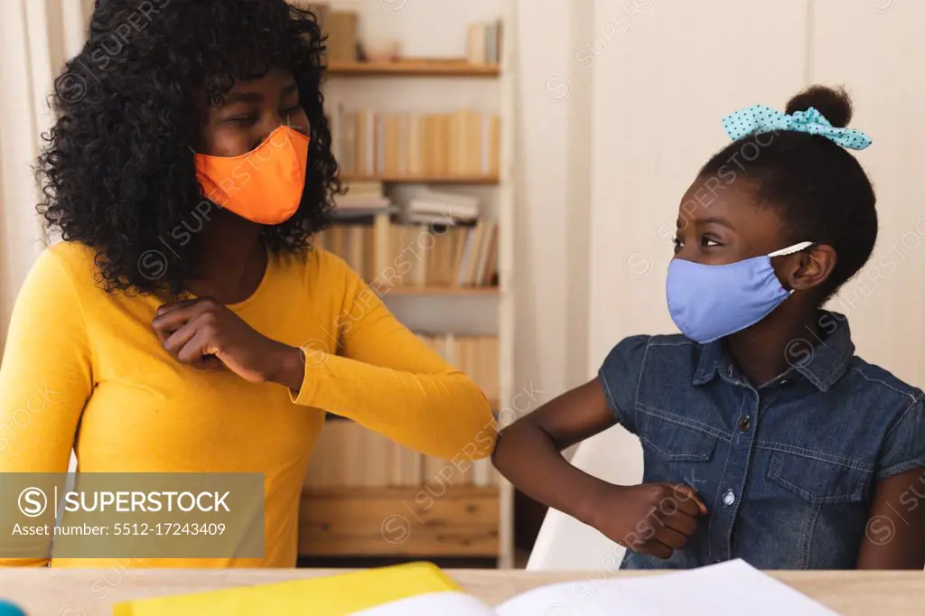 African american mother and daughter wearing face mask greeting each other by touching elbows at home. social distancing during covid 19 coronavirus quarantine lockdown.