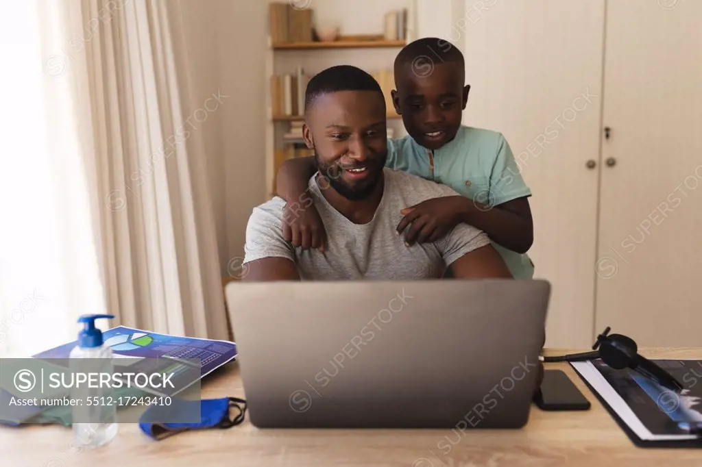 African american father and son having a video chat on laptop at home. social distancing during covid 19 coronavirus quarantine lockdown.
