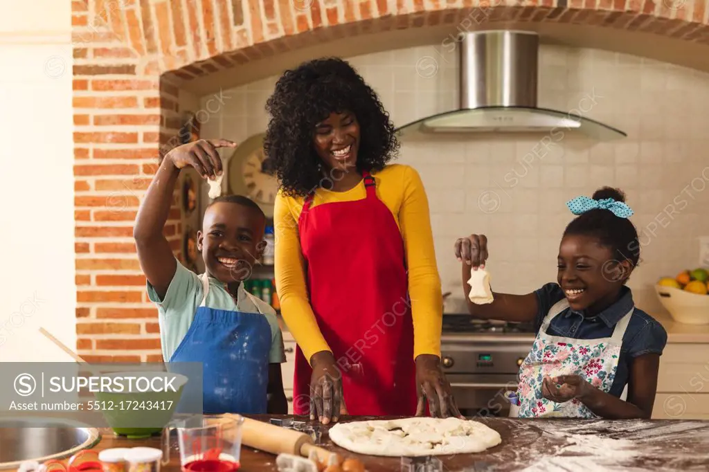 African american mother, son and daughter baking together and holding pieces of dough in the kitchen at home. christmas festivity tradition celebration concept
