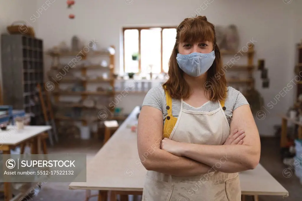 Portrait of caucasian woman wearing face mask at pottery studio. small creative business during covid 19 coronavirus pandemic.