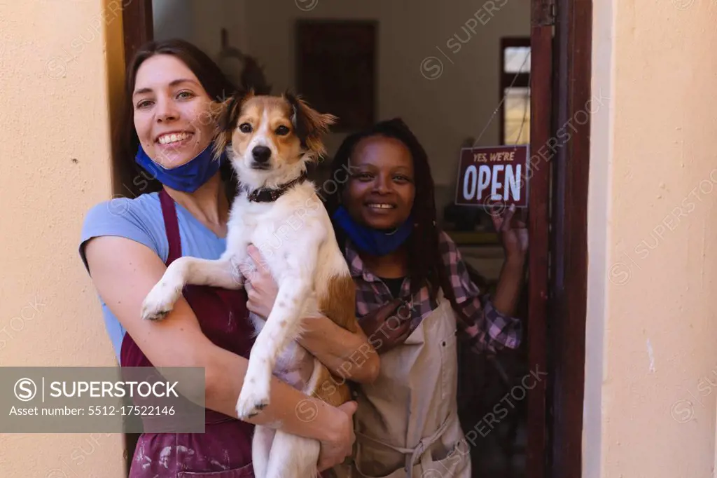 Portrait of caucasian and mixed race women at pottery studio, holding a puppy. small creative business during covid 19 coronavirus pandemic.