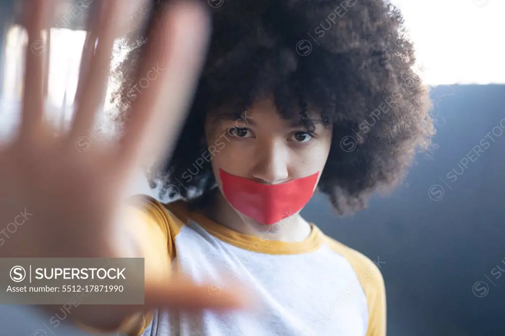 Mixed race woman with tape on mouth looking at camera holding her arm straight. gender fluid lgbt identity racial equality concept.