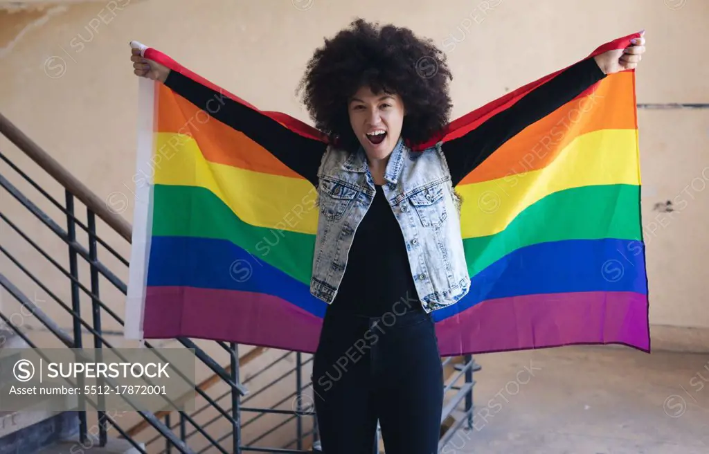 Mixed race woman holding rainbow flag shouting to camera. gender fluid lgbt identity racial equality concept.