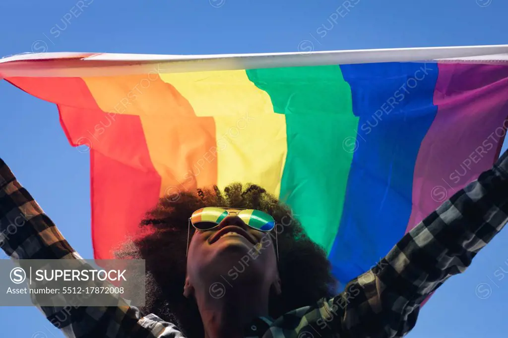 Mixed race woman standing on rooftop holding rainbow flag. gender fluid lgbt identity racial equality concept.