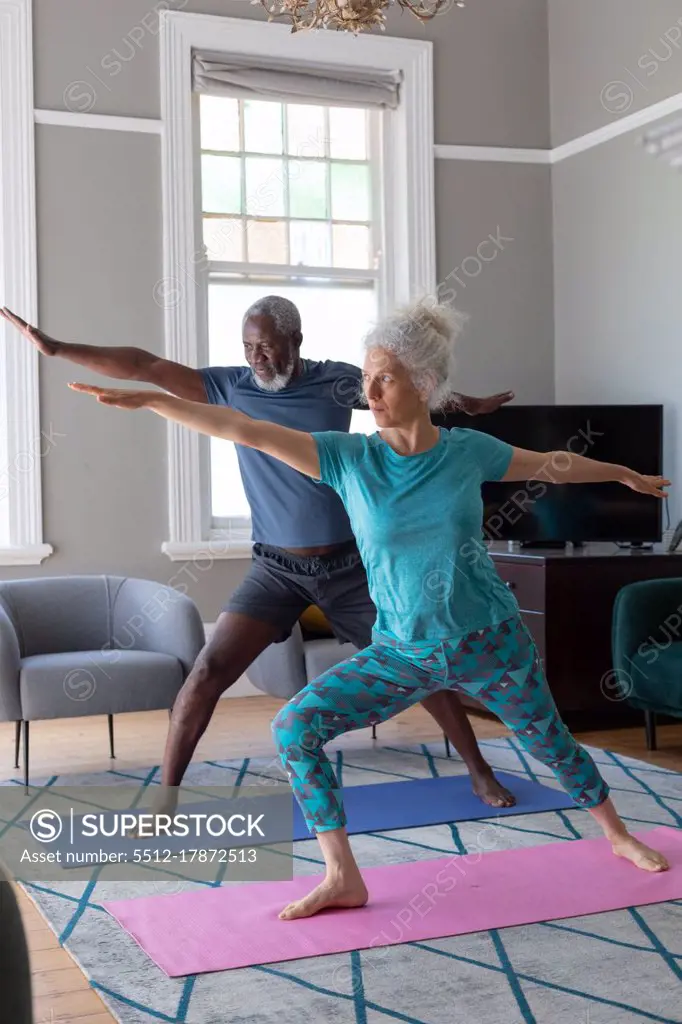 Senior mixed race couple wearing sports clothes exercising in living room. staying at home in self isolation during quarantine lockdown.