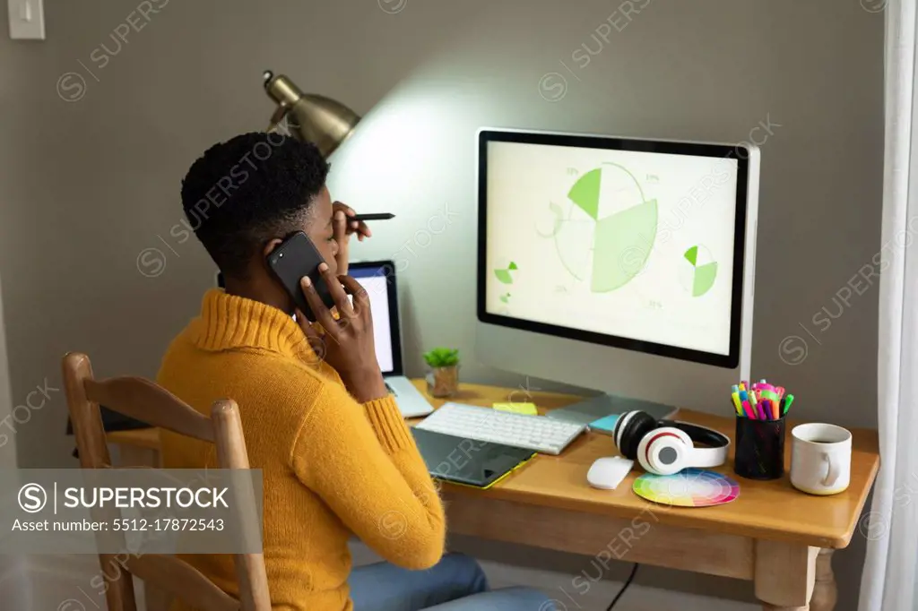 African american woman talking on smartphone and using computer while working from home. staying at home in self isolation in quarantine lockdown