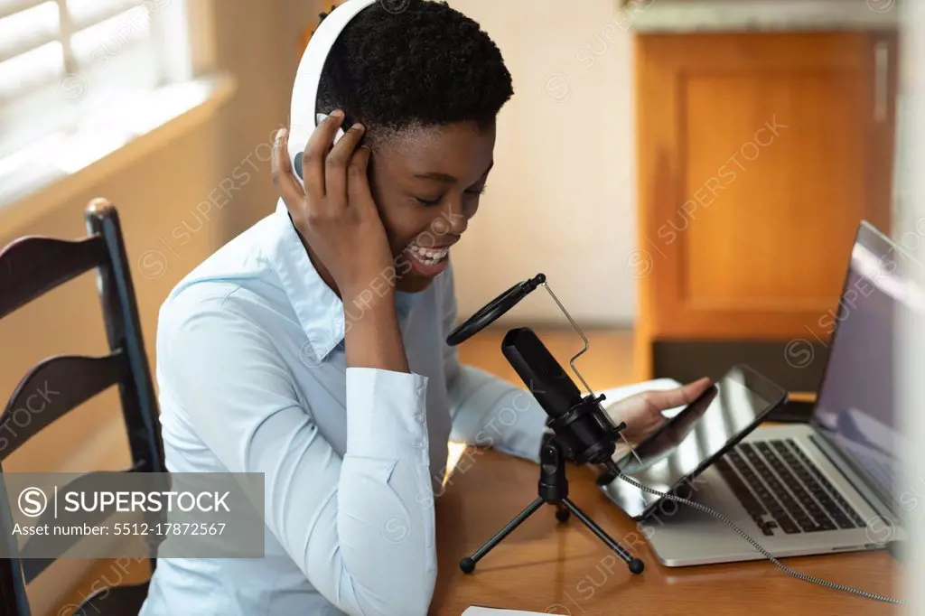 African american woman wearing headphones using microphone and laptop. communication online, staying at home in self isolation during quarantine lockdown.