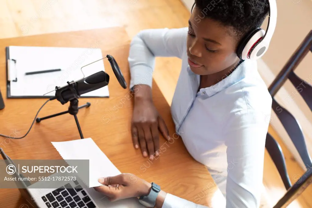 African american woman wearing headphones using microphone and laptop. communication online, staying at home in self isolation during quarantine lockdown.