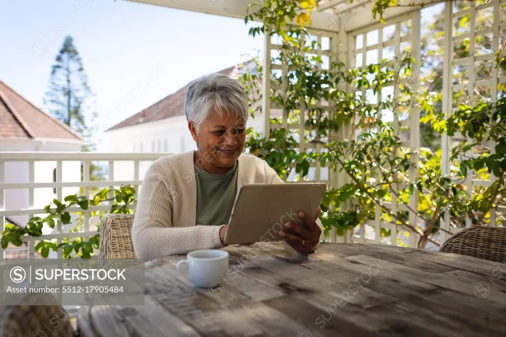 Senior african american woman sitting by table using digital tablet drinking coffee on terrace. retirement lifestyle in self isolation during quarantine lockdown.