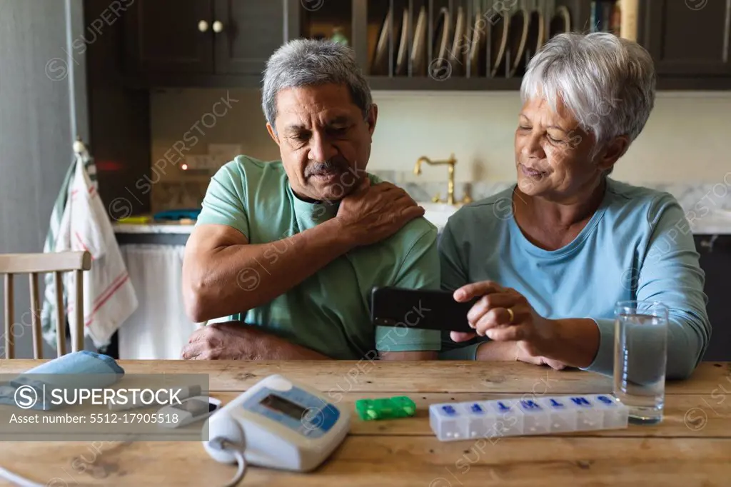 Senior african american couple sitting by table using smartphone. retirement lifestyle in self isolation during quarantine lockdown.