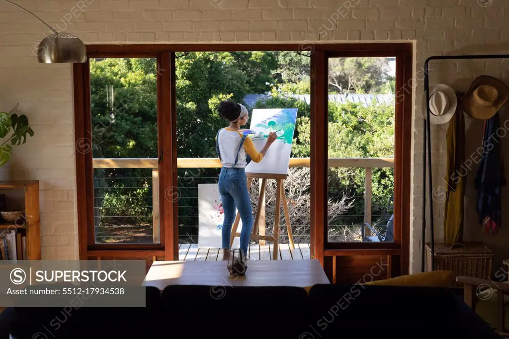 Caucasian woman painting picture standing on sunny terrace. Staying at home in self isolation during quarantine lockdown.