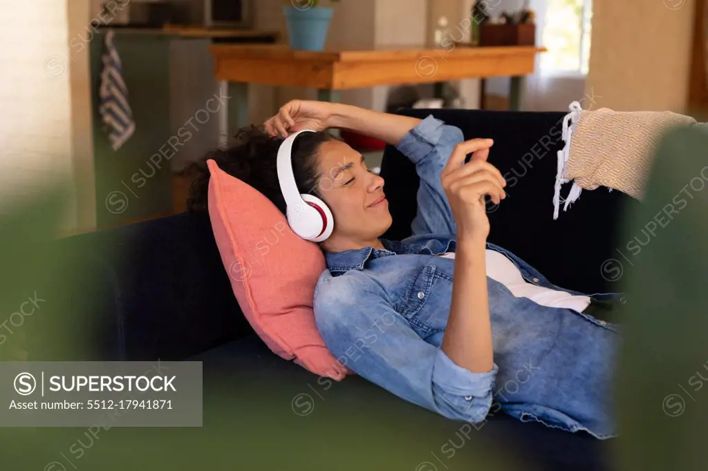 Caucasian woman lying on sofa with headphones on, relaxing at home. Staying at home in self isolation during quarantine lockdown.