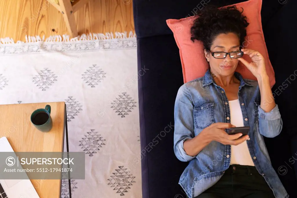 Caucasian woman lying on sofa with holding smartphone, relaxing at home. Staying at home in self isolation during quarantine lockdown.
