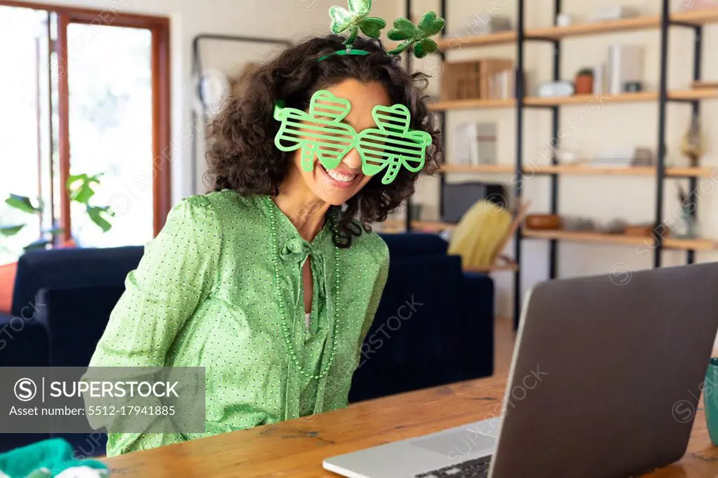 Caucasian woman dressed in green with shamrock glasses making st patrick's day video call. staying at home in self isolation during quarantine lockdown.