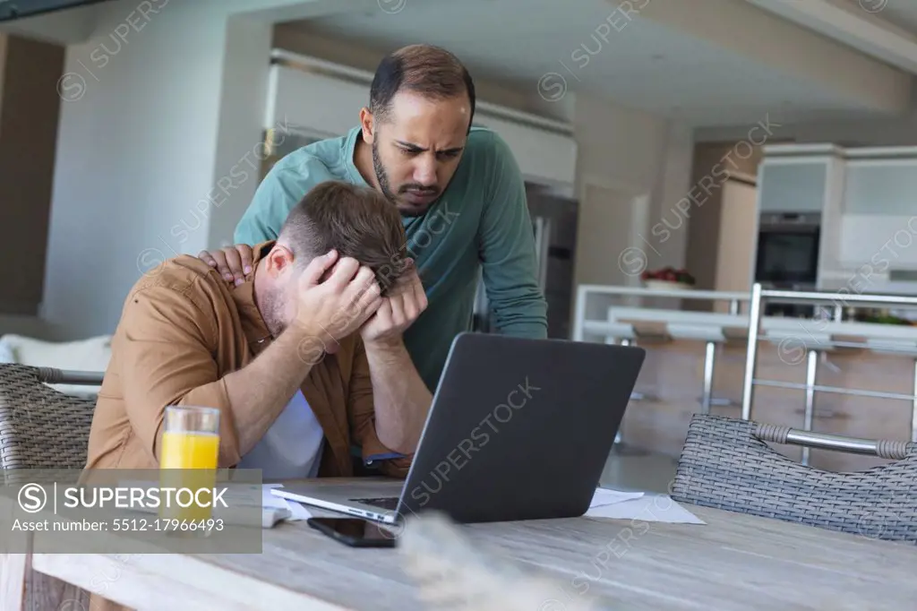 Worried multi ethnic gay male couple going through bills and using laptop at home. staying at home in self isolation during quarantine lockdown.