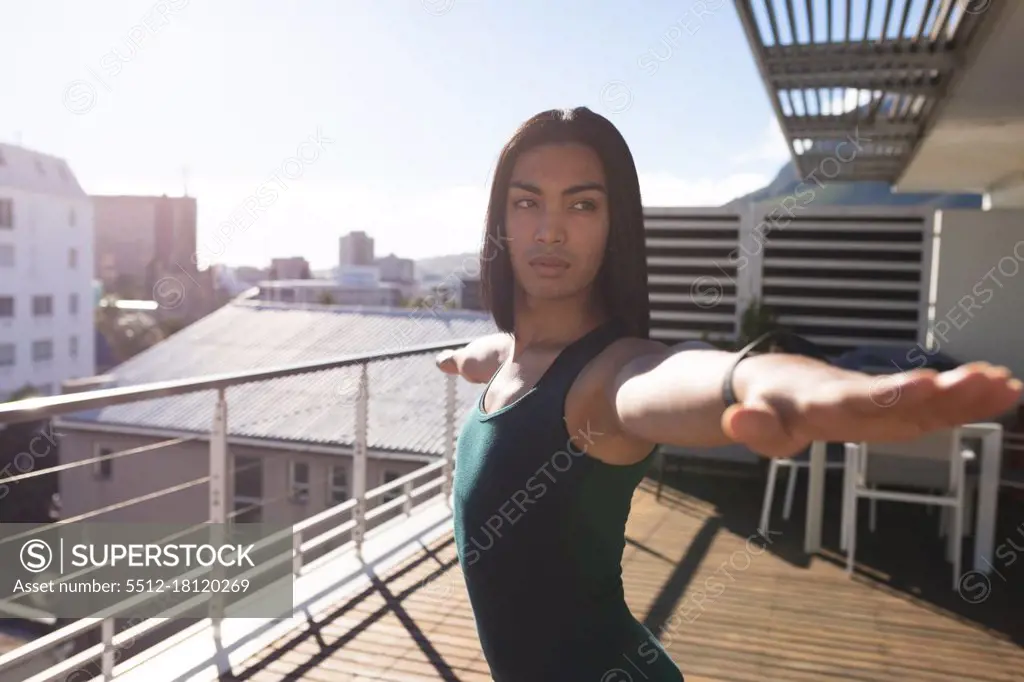 Mixed race transgender woman practicing yoga standing on roof terrace in the sun. staying at home in isolation during quarantine lockdown.