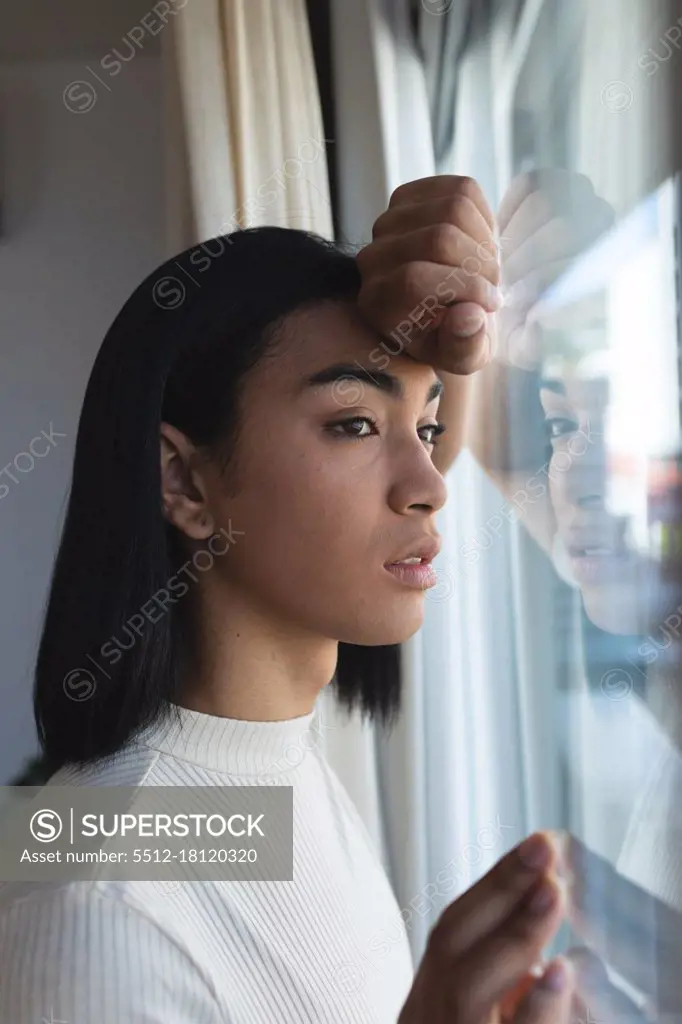 Mixed race transgender woman looking out of window in thought on sunny day. staying at home in isolation during quarantine lockdown.