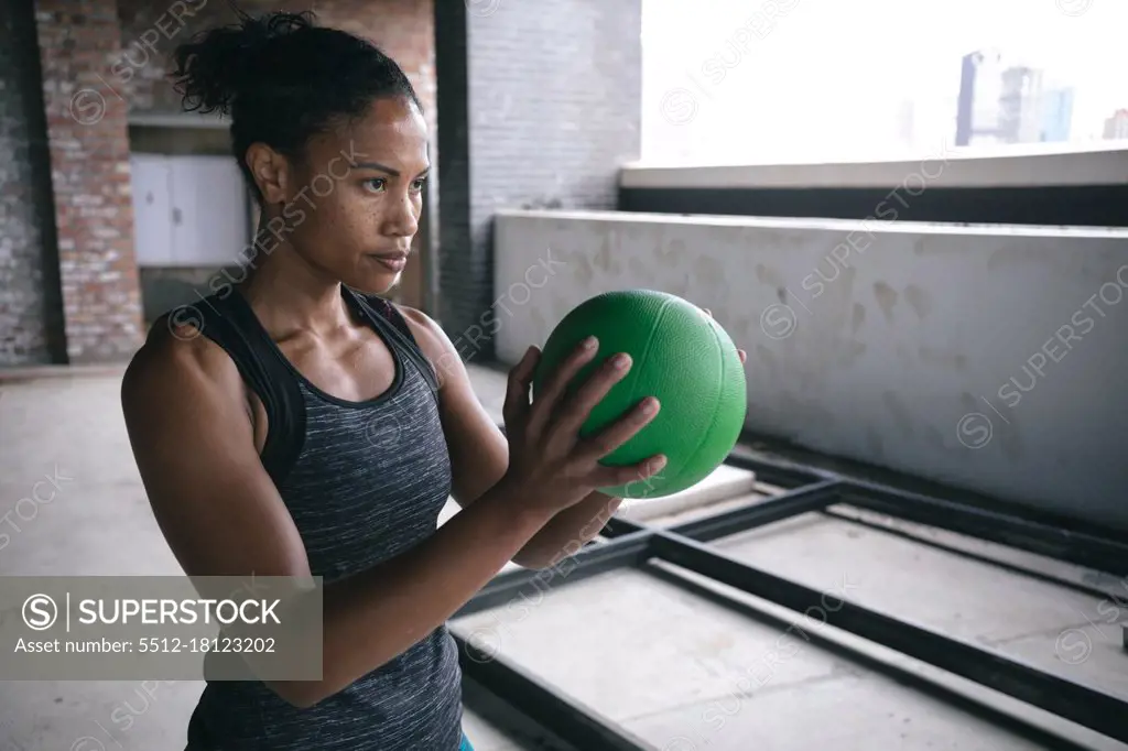 Determined fit african american woman exercising holding volleyball ball in empty warehouse space. urban fitness and sport.