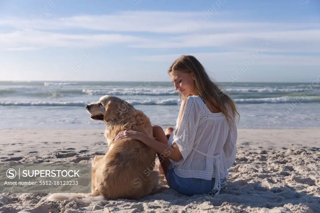 Caucasian woman sitting on sand petting a dog at the beach. healthy outdoor leisure time by the sea.