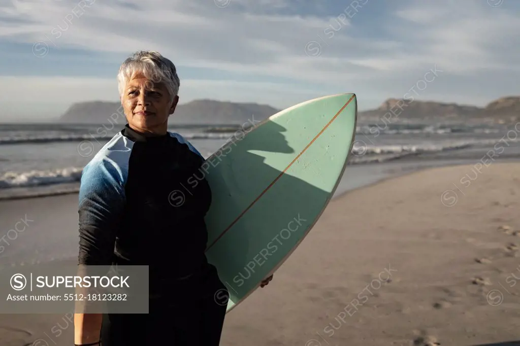 Senior african american woman holding surf board standing on the beach. travel vacation retirement lifestyle concept