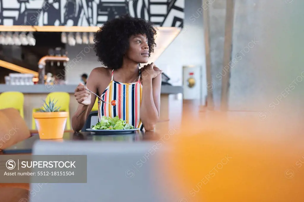 African american woman sitting at table and eating in restaurant. independent cafe, small successful business.