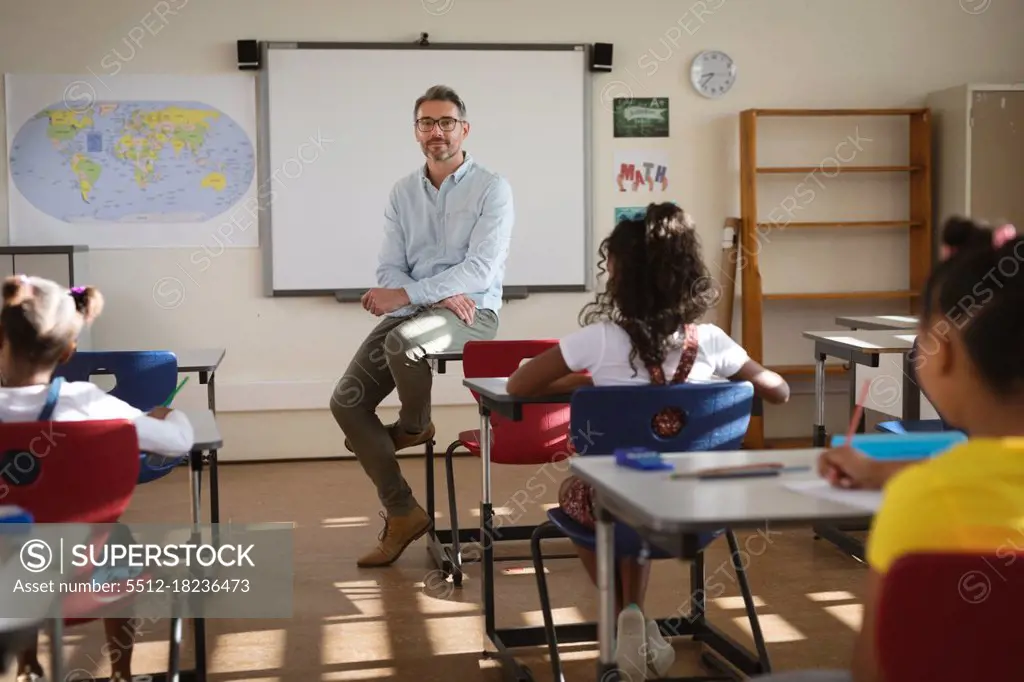 Portrait of caucasian male teacher teaching diverse group of students in class at elementary school. school and education concept
