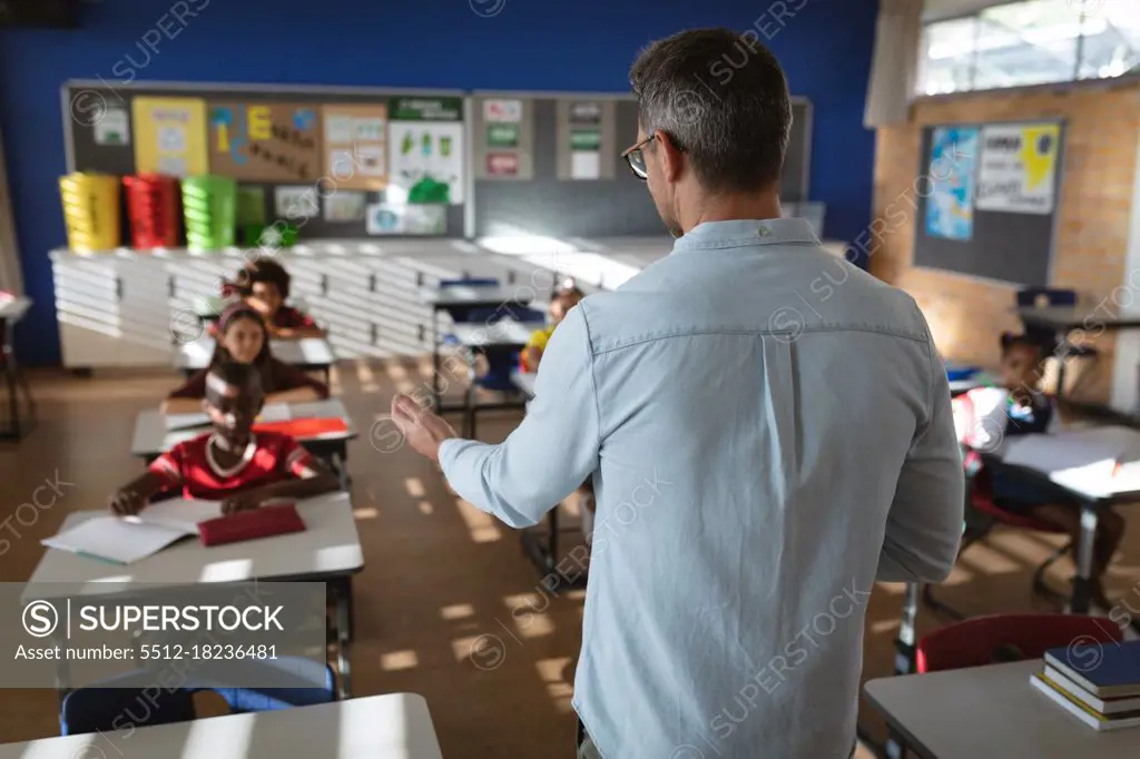 Rear view of caucasian male teacher teaching to diverse students in the class at elementary school. school and education concept