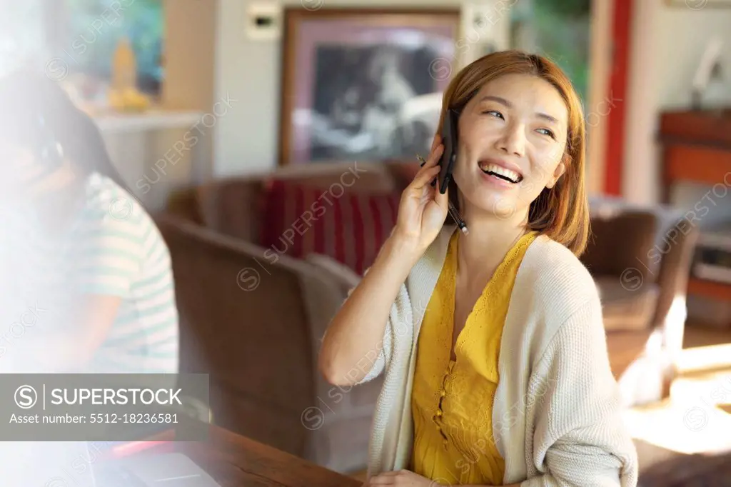 Smiling asian woman talking on smartphone, working from home. at home in isolation during quarantine lockdown.