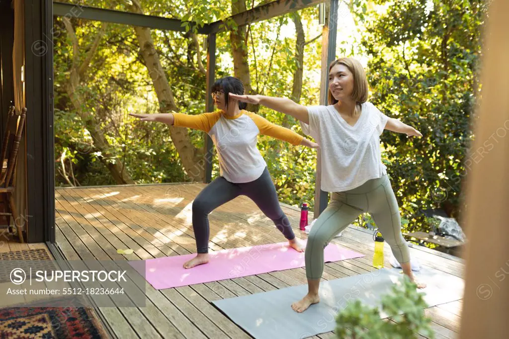 Smiling asian woman and her daughter practicing yoga on terrace in garden. at home in isolation during quarantine lockdown.