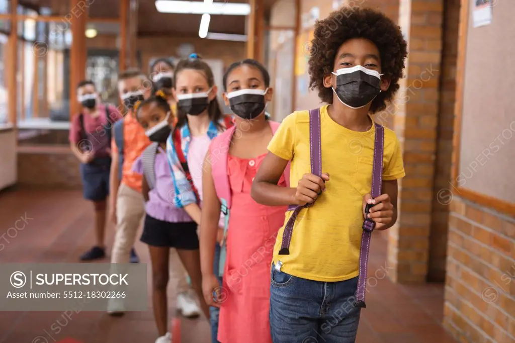 Portrait of group of diverse students wearing face masks while standing in the corridor at school. hygiene and social distancing at school during covid 19 pandemic
