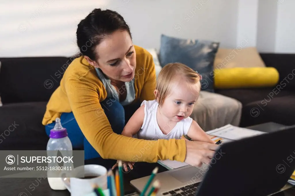 Caucasian mother holding her baby using laptop while working from home. motherhood, love and baby care concept