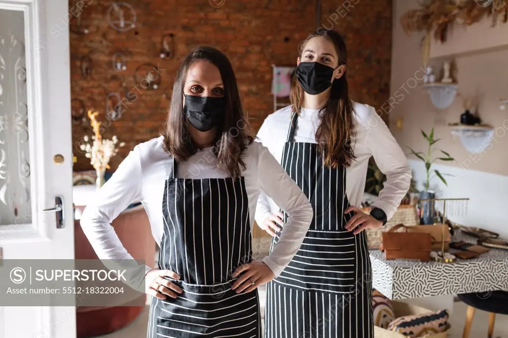 Caucasian business owner and waitress wearing face masks and aprons, looking at camera. small independent cafe business during coronavirus covid 19 pandemic.