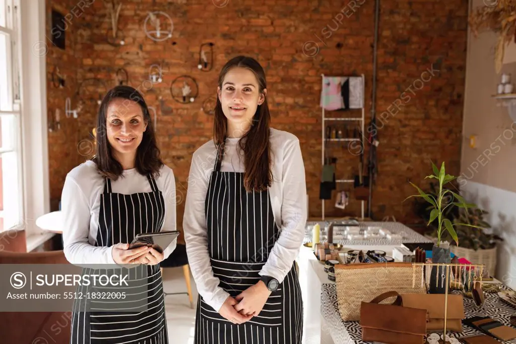 Caucasian business owner and waitress wearing aprons, looking at camera, smiling. small independent cafe business.