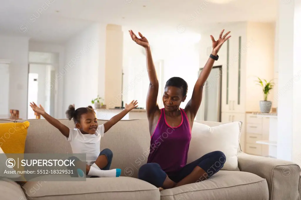 Happy african american mother and daughter practicing yoga, sitting on couch in living room. family spending time together at home.