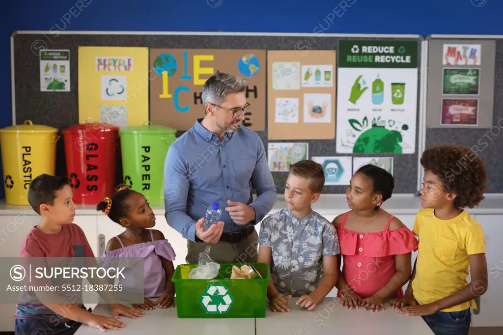 Caucasian male teacher teaching group of diverse students to recycle plastic items at school. school and education concept