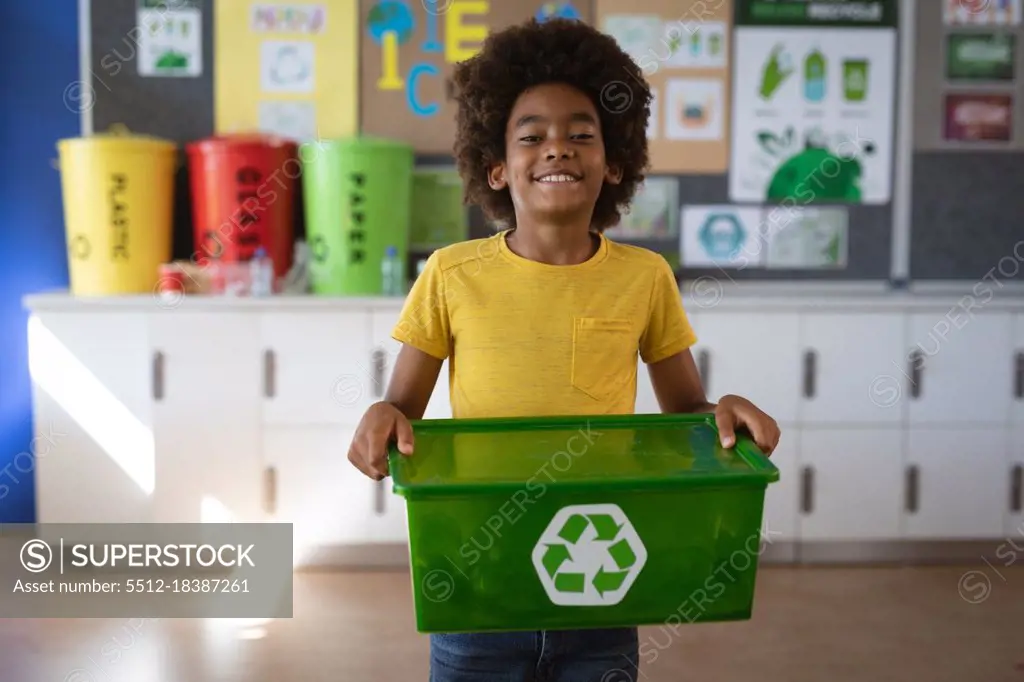 Portrait of african american boy holding tray filled with recyclable plastic items at school. school and education concept
