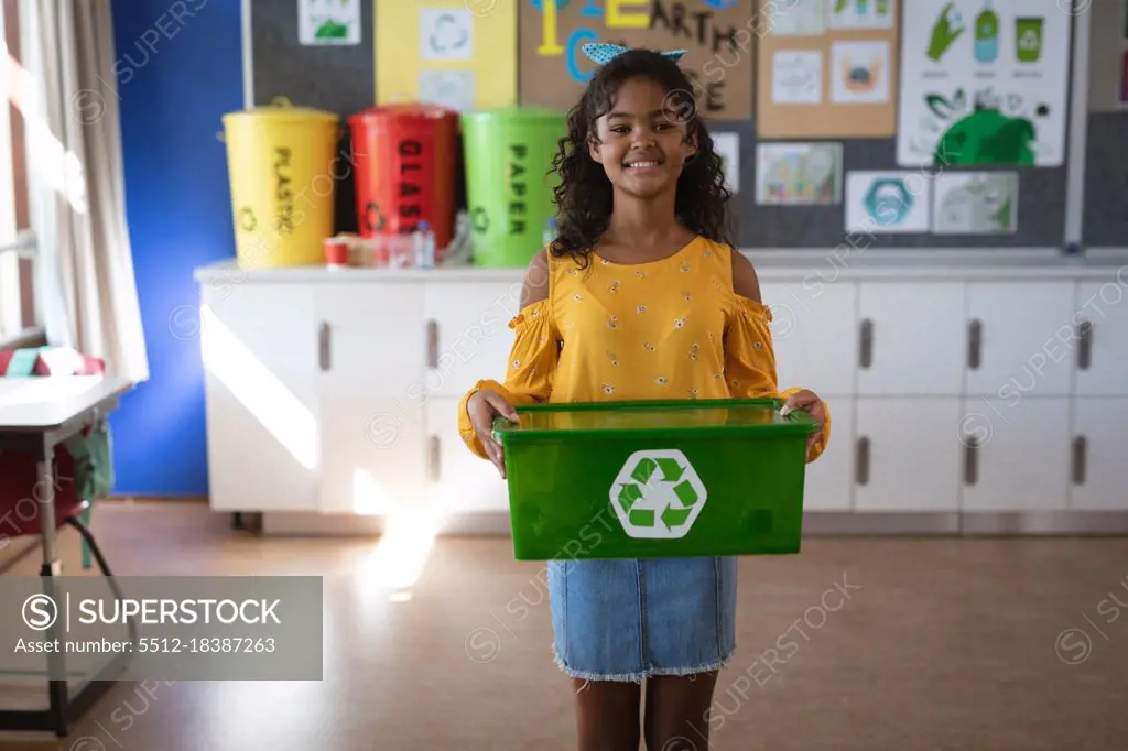 Portrait of african american girl holding tray filled with recyclable plastic items at school. school and education concept