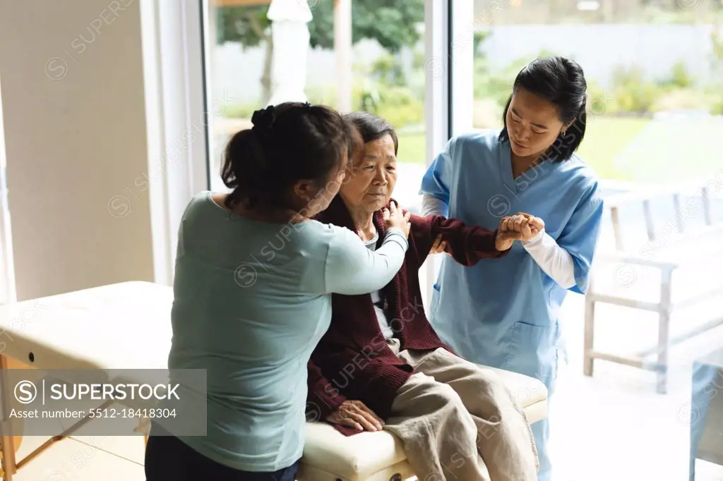 Asian female physiotherapist and daughter treating senior female patient at her home. healthcare and medical physiotherapy treatment.