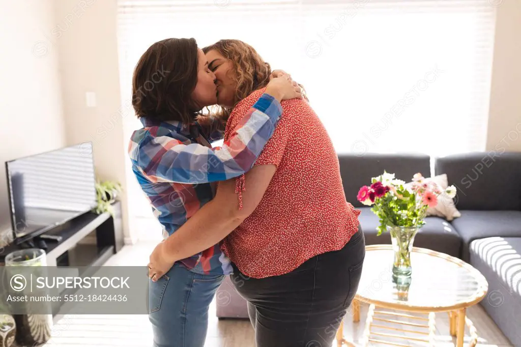 Happy lesbian couple embracing and kissing in living room. domestic lifestyle, spending free time at home.