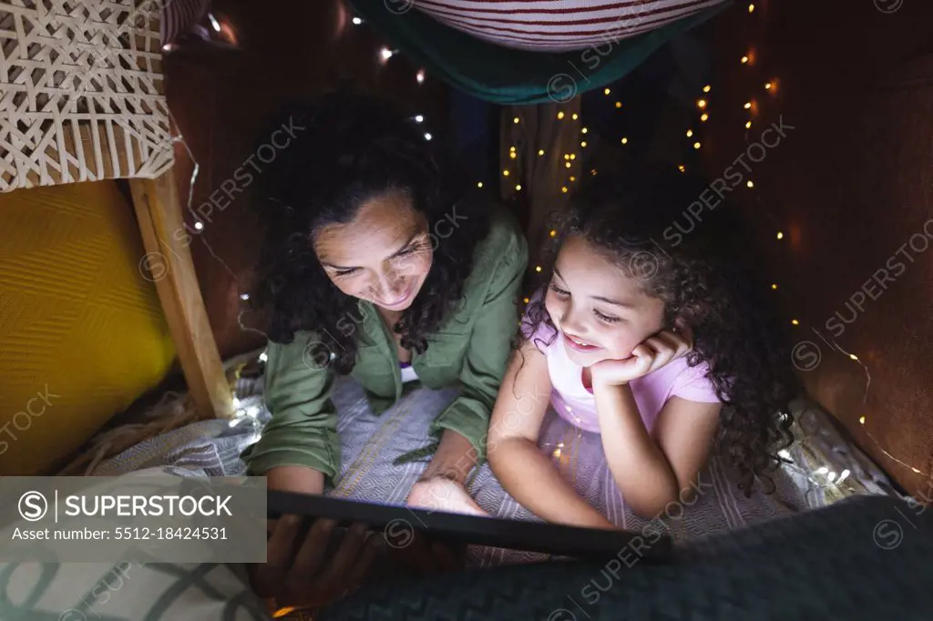 Happy mixed race mother and daughter using laptop in makeshift tent. domestic lifestyle and spending quality time at home.