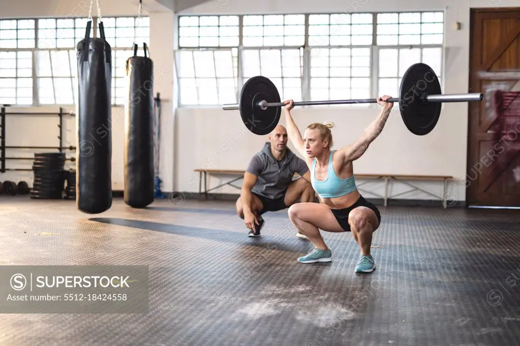 Caucasian male trainer instructing woman exercising at gym, lifting weights. strength and fitness cross training for boxing.