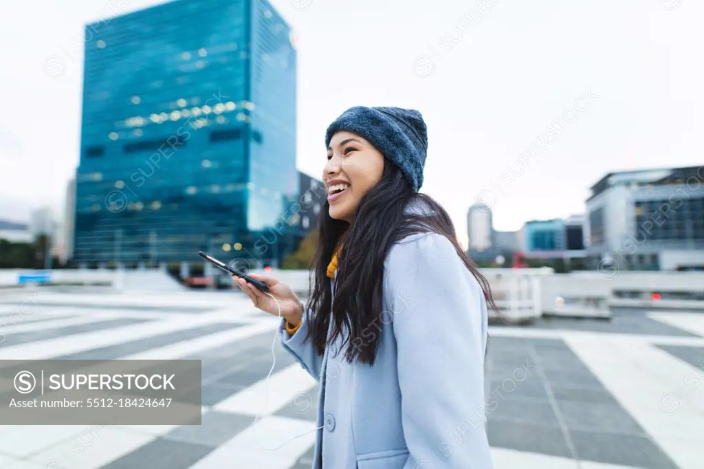 Asian woman smiling and using smartphone in the street. independent young woman out and about in the city.