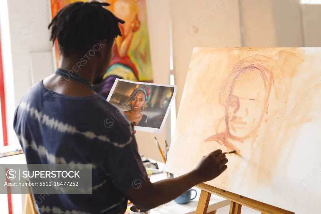 African american male painter at work painting portrait on canvas in art studio. creation and inspiration at an artists painting studio.