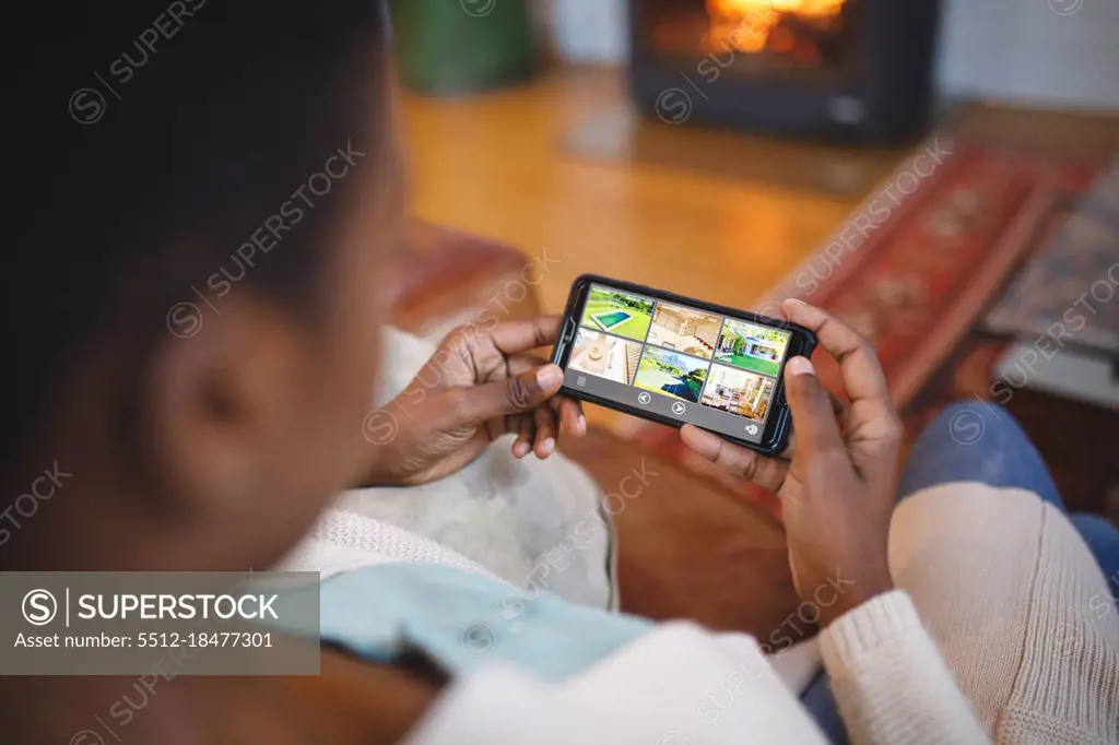 African american woman in living room sitting on sofa and using smartphone. domestic lifestyle, enjoying leisure time at home.