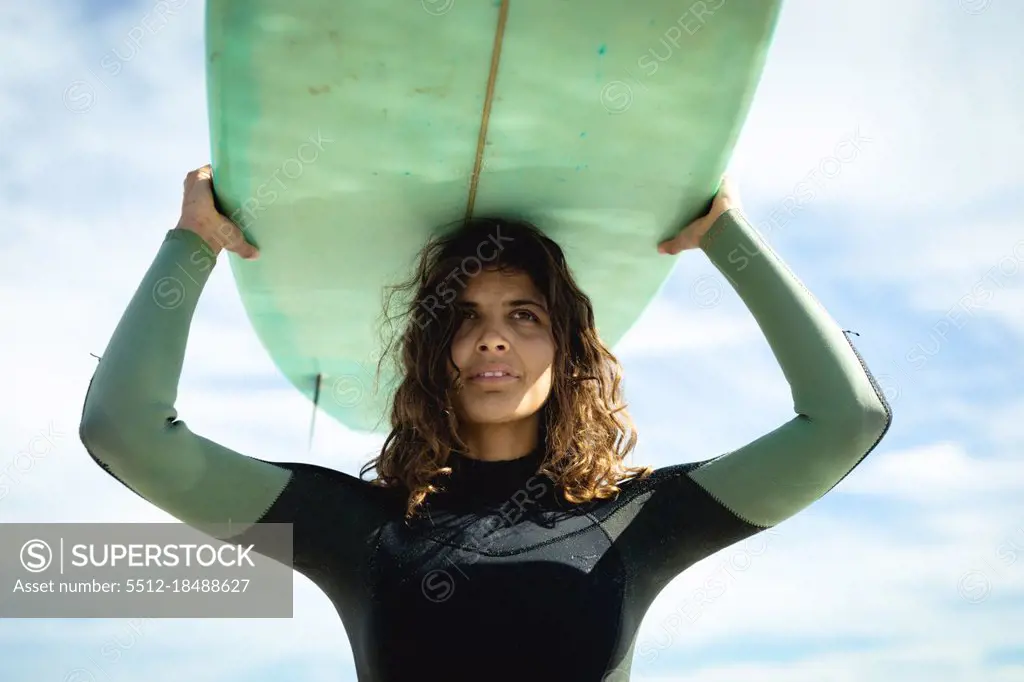 Mixed race woman holding surfboard on sunny day at beach. healthy lifestyle, enjoying leisure time outdoors.